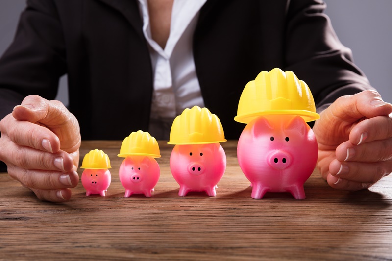 Businessperson Protecting Piggybanks With Yellow Hardhat